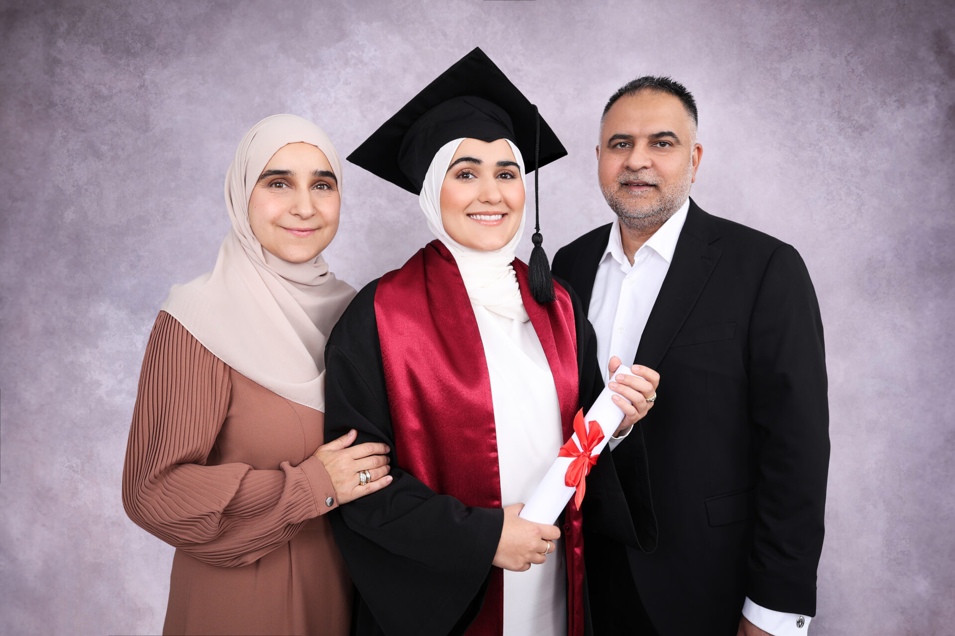 Mother, father and daughter during graduation photoshoot London with gown, mortarboard and hat in professional studio London.