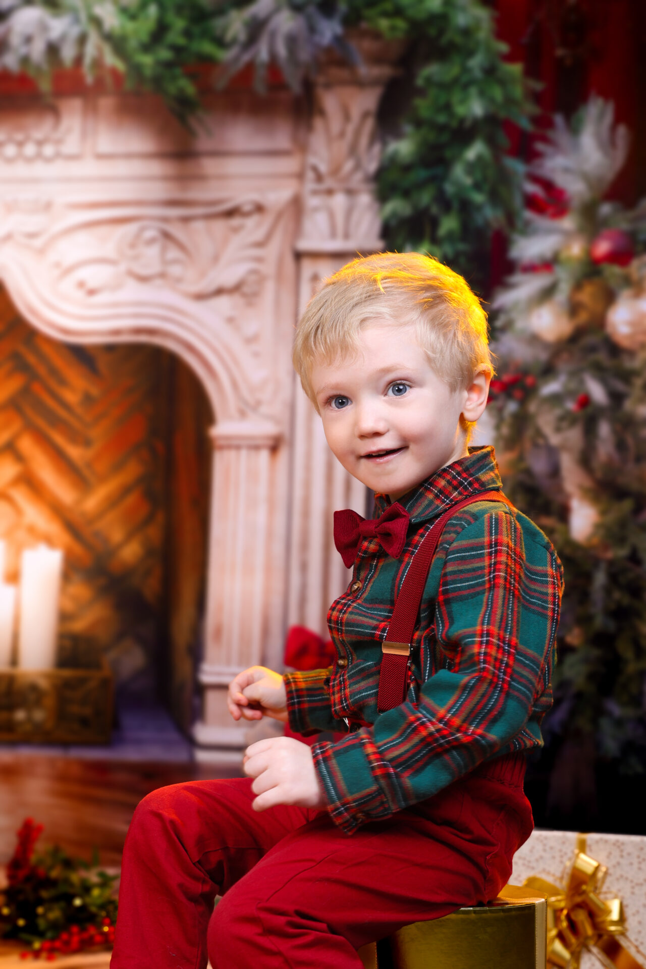 Kid sitting on a chair agaist festive christmas backdrop fireplace.