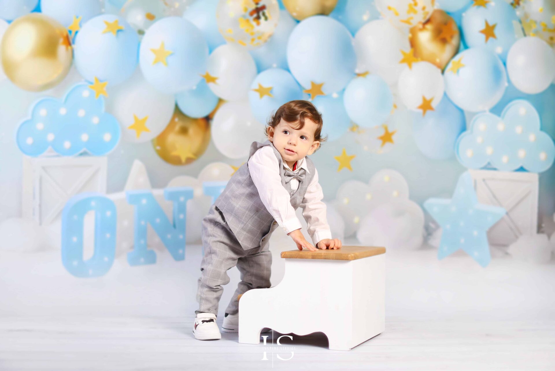 Baby boy smiling in a cloud-themed first birthday photoshoot with blue and gold balloon decor.