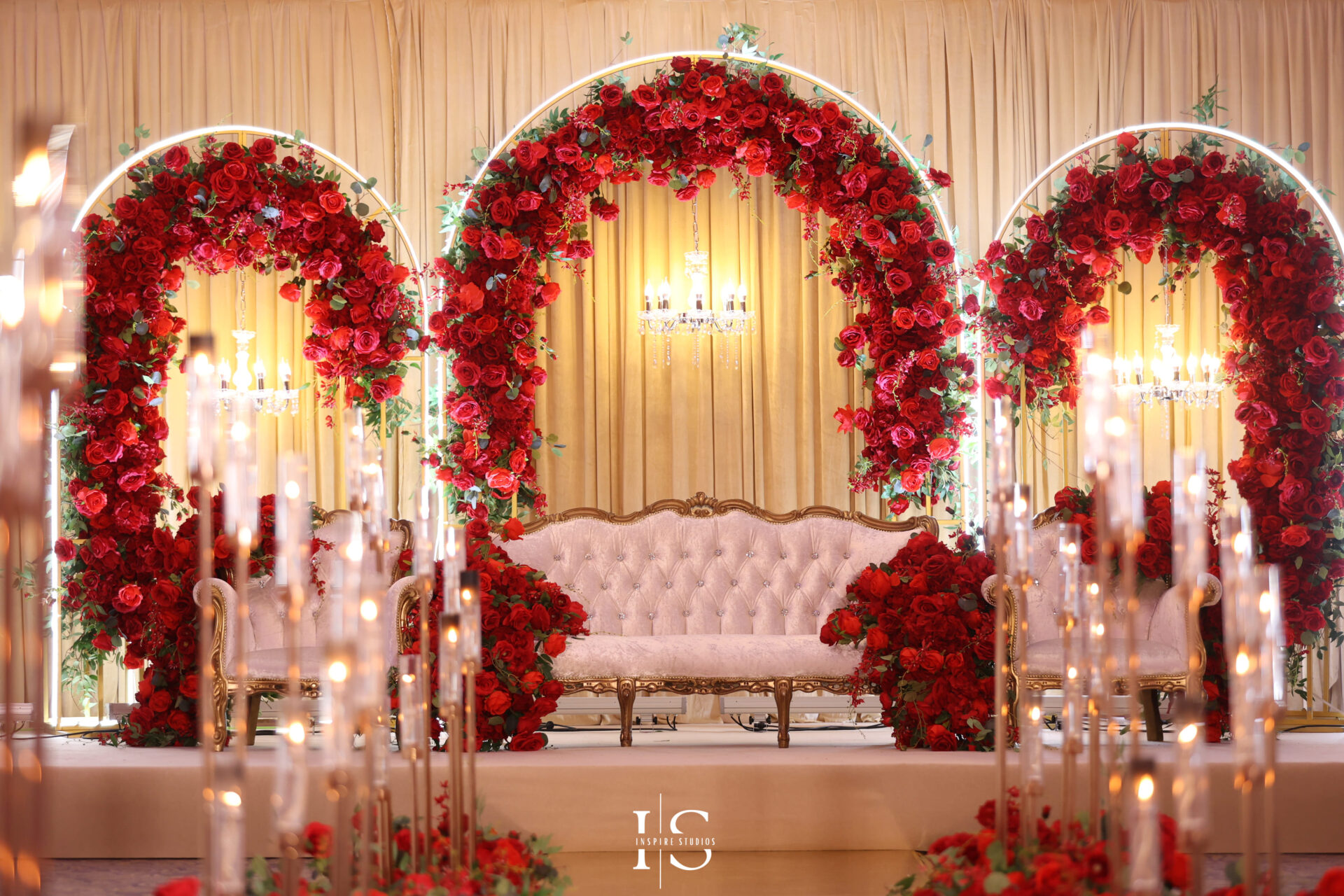 Luxurious London baraat wedding stage decorated with red roses, chandeliers, and a white tufted sofa.