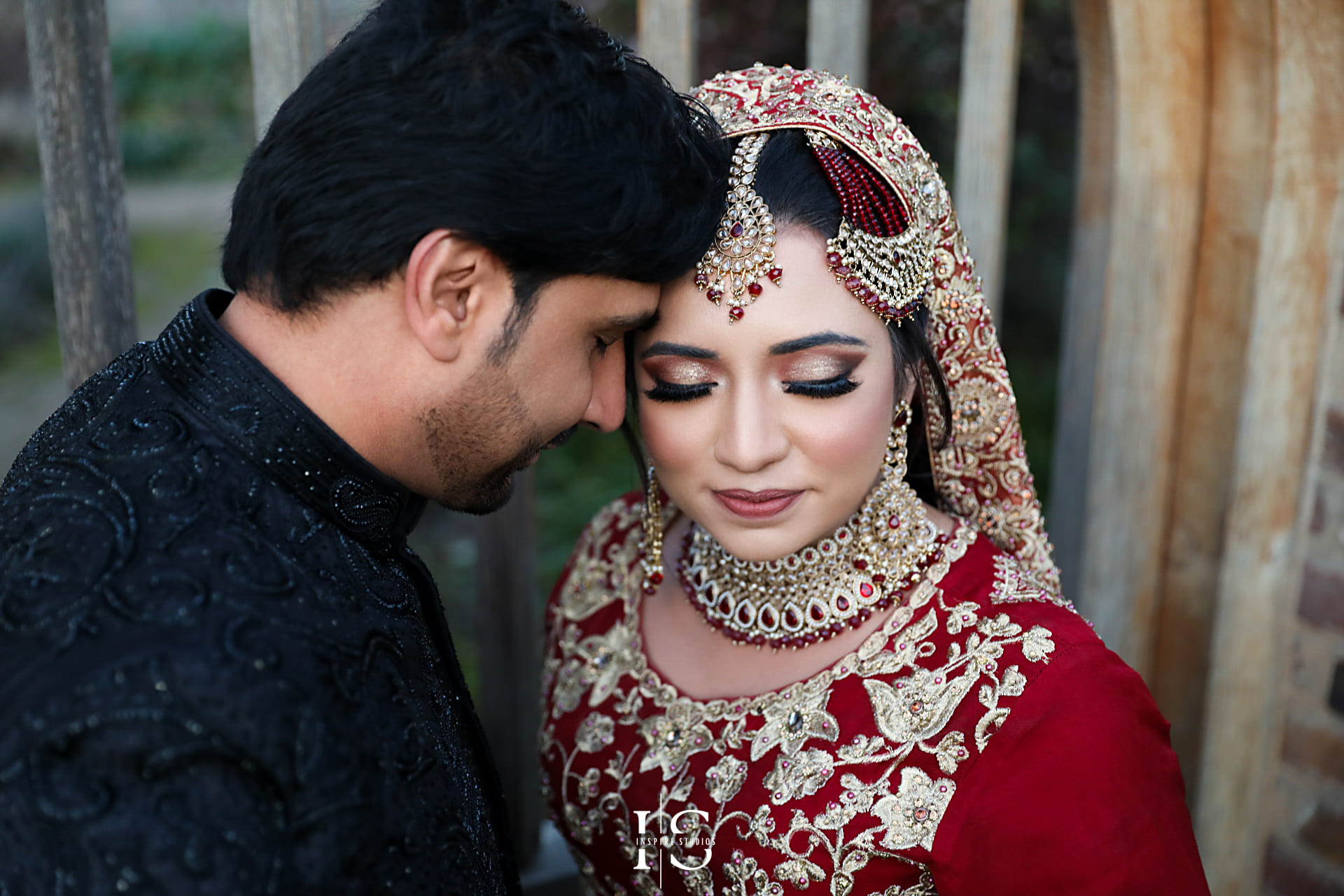 A bride in a red embroidered lehenga and groom in a black sherwani sharing a romantic moment during their baraat wedding in London.