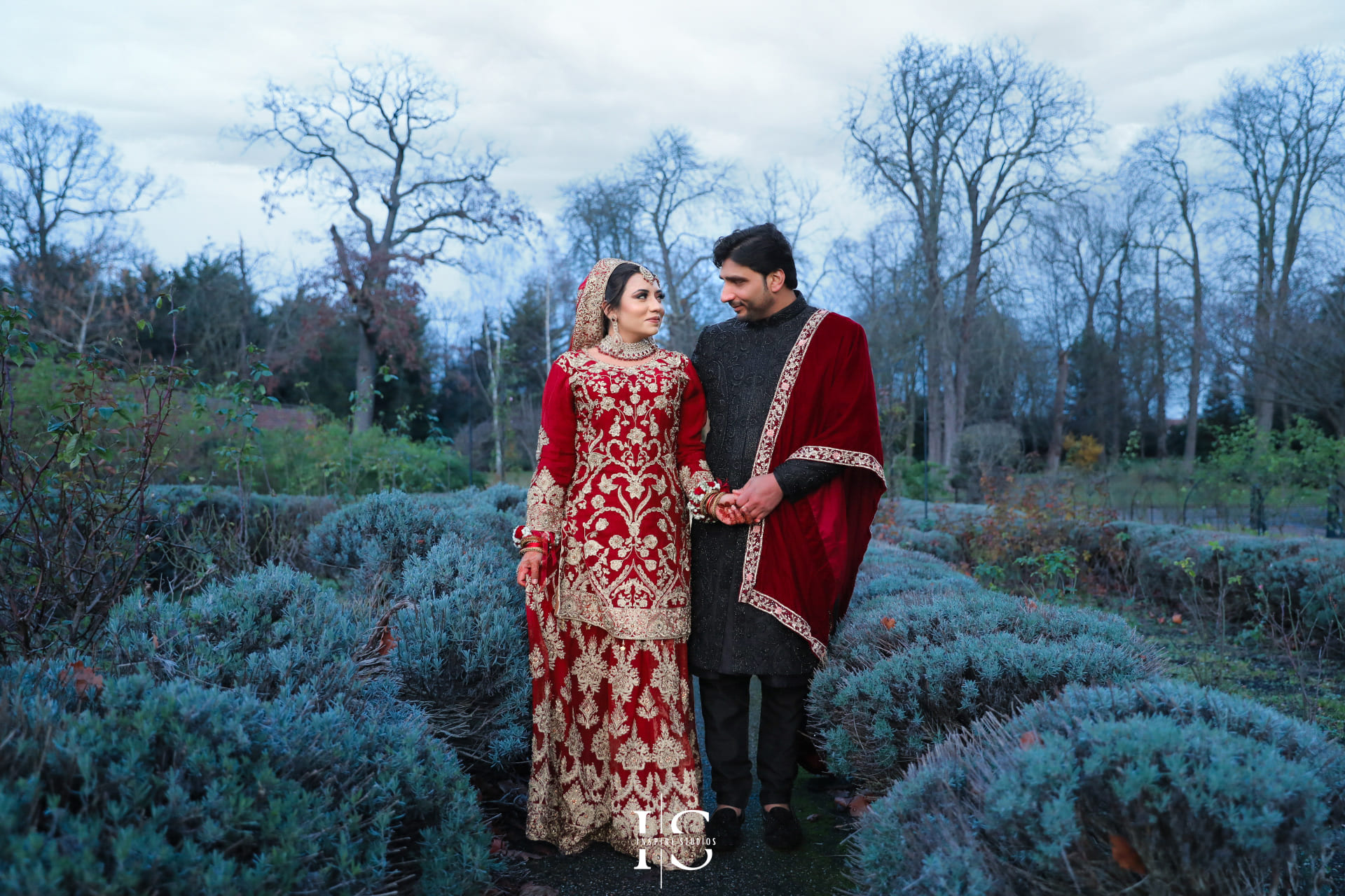 A bride in a red embroidered lehenga and groom in a black sherwani sharing a romantic moment during their baraat wedding in London.