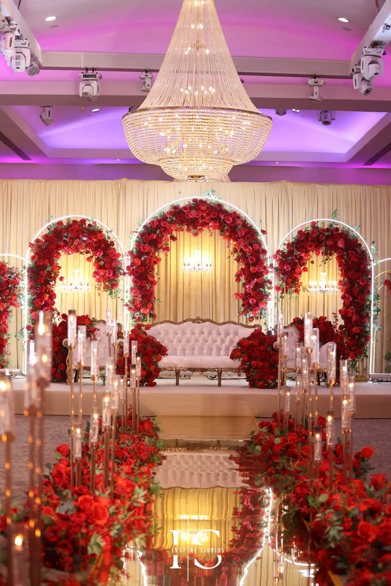 Luxurious London walima wedding stage in Meridian Grand, decorated with red roses, chandeliers, and a white tufted sofa.