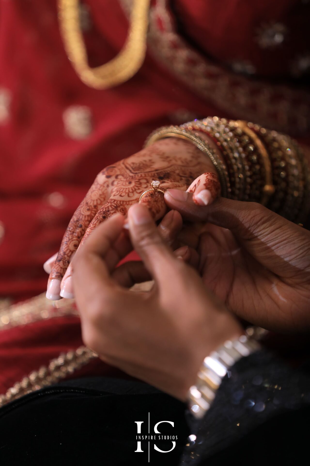 A close-up of a groom placing a diamond ring on the bride's hand, adorned with henna and gold bangles during a baraat wedding in London.