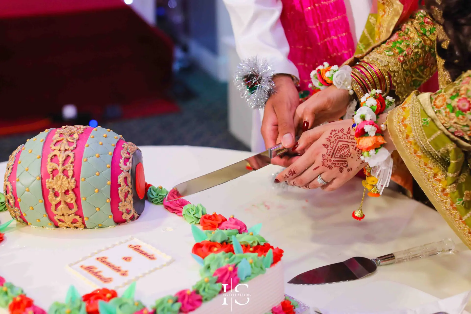Bride is cutting the Mehndi cake with her family. This cake is usually a real beauty, is layered in the shape of a dholl or as a beautiful and colourful cake with mehndi decorations like a veil or henna cons.