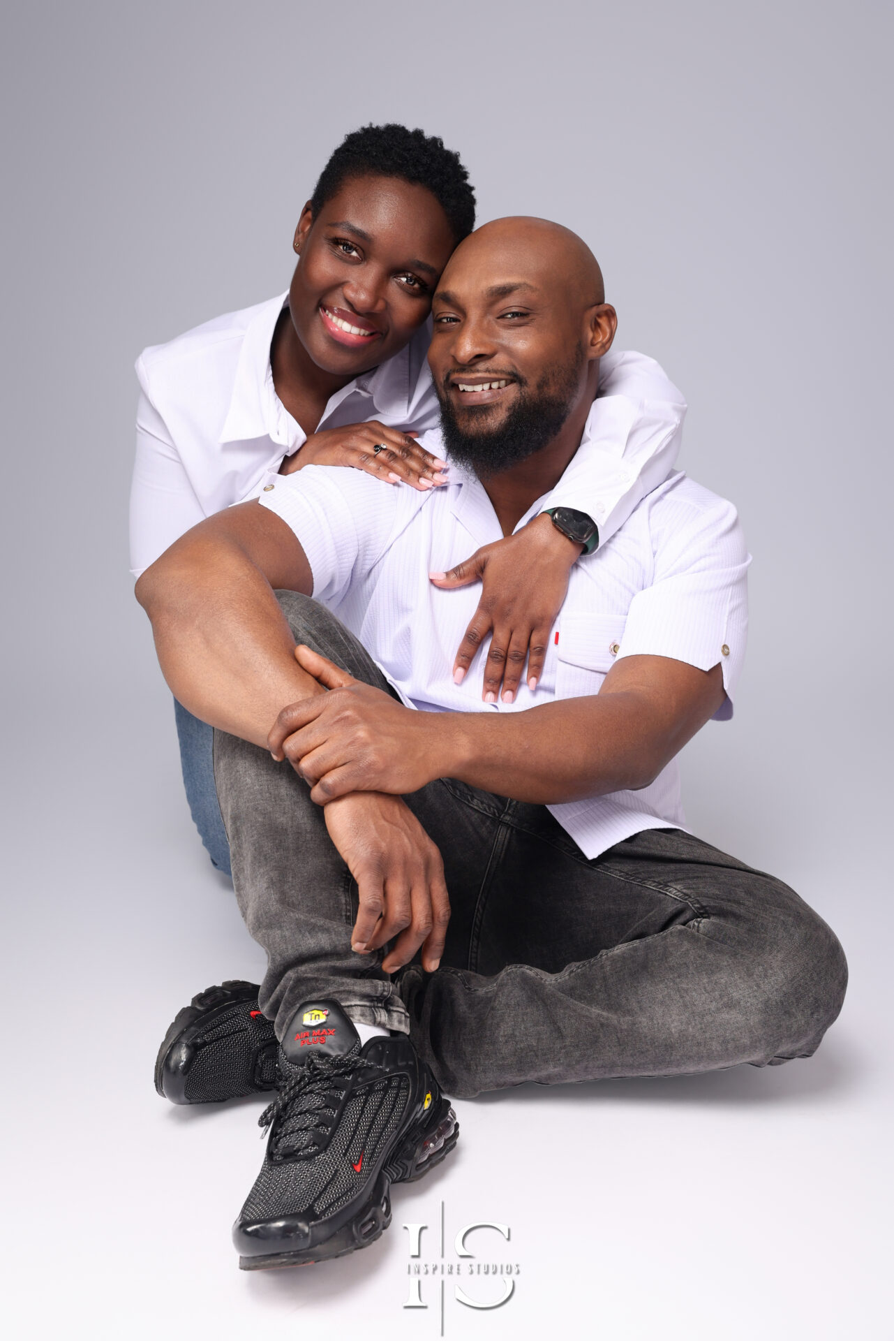 A couple dressed in sophisticated evening wear shares a tender moment in a high-end London studio photoshoot.