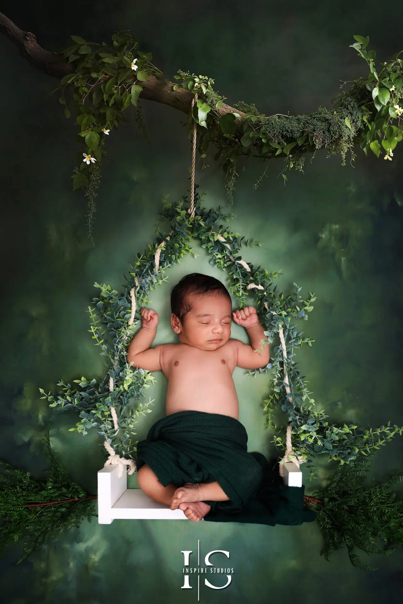 Newborn baby boy posed on a decorative swing in a studio setting.