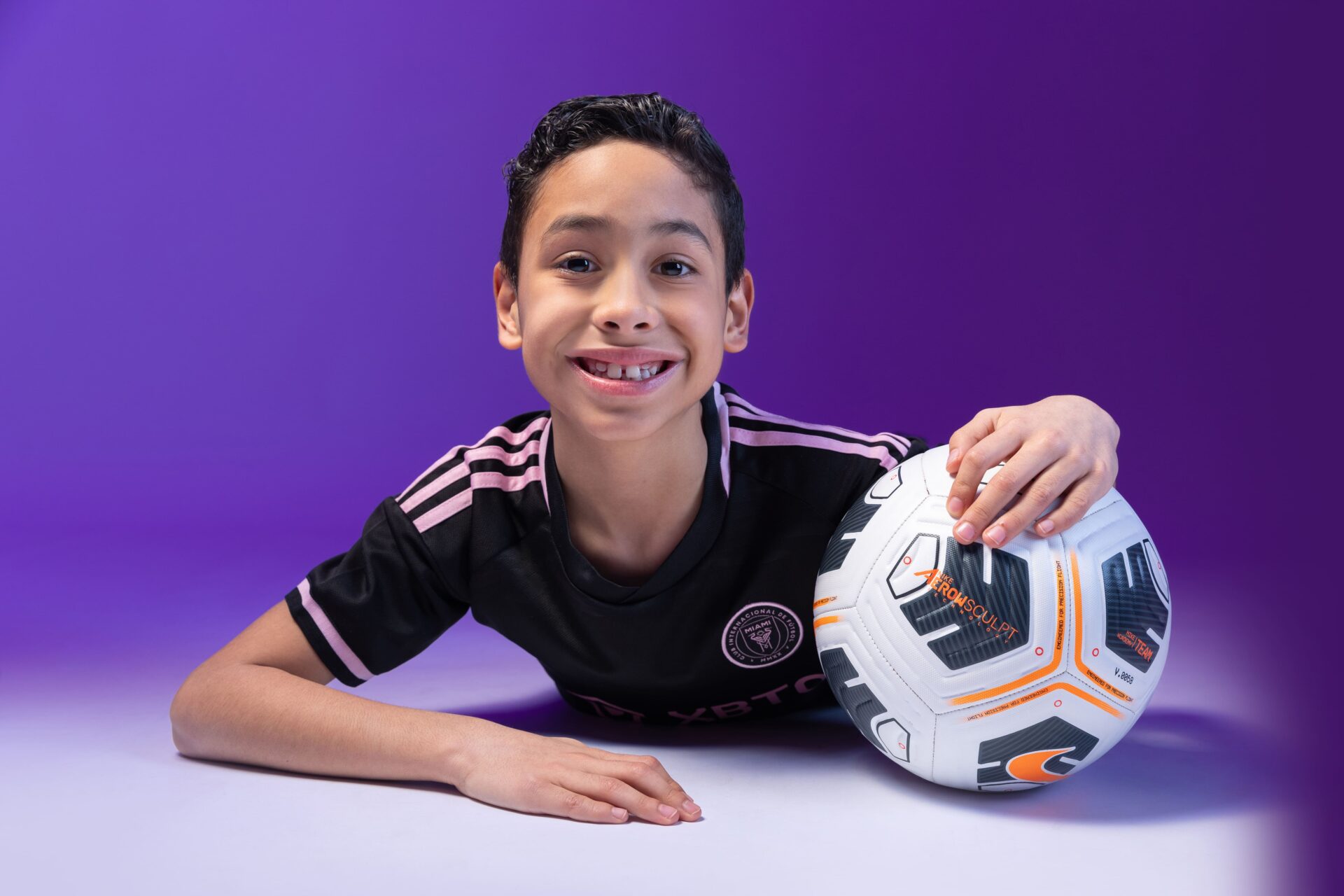 Child posing for a football-themed portrait with colourful studio lights.