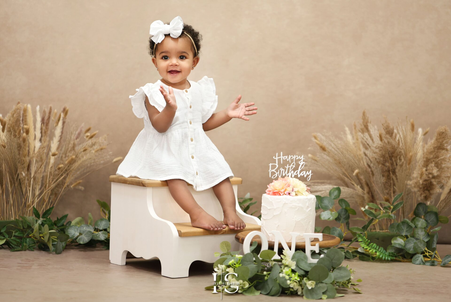 Adorable one-year-old baby enjoying a boho-themed cake smash photoshoot in East London studio, with neutral tones, natural props, and a rustic birthday cake setup.
