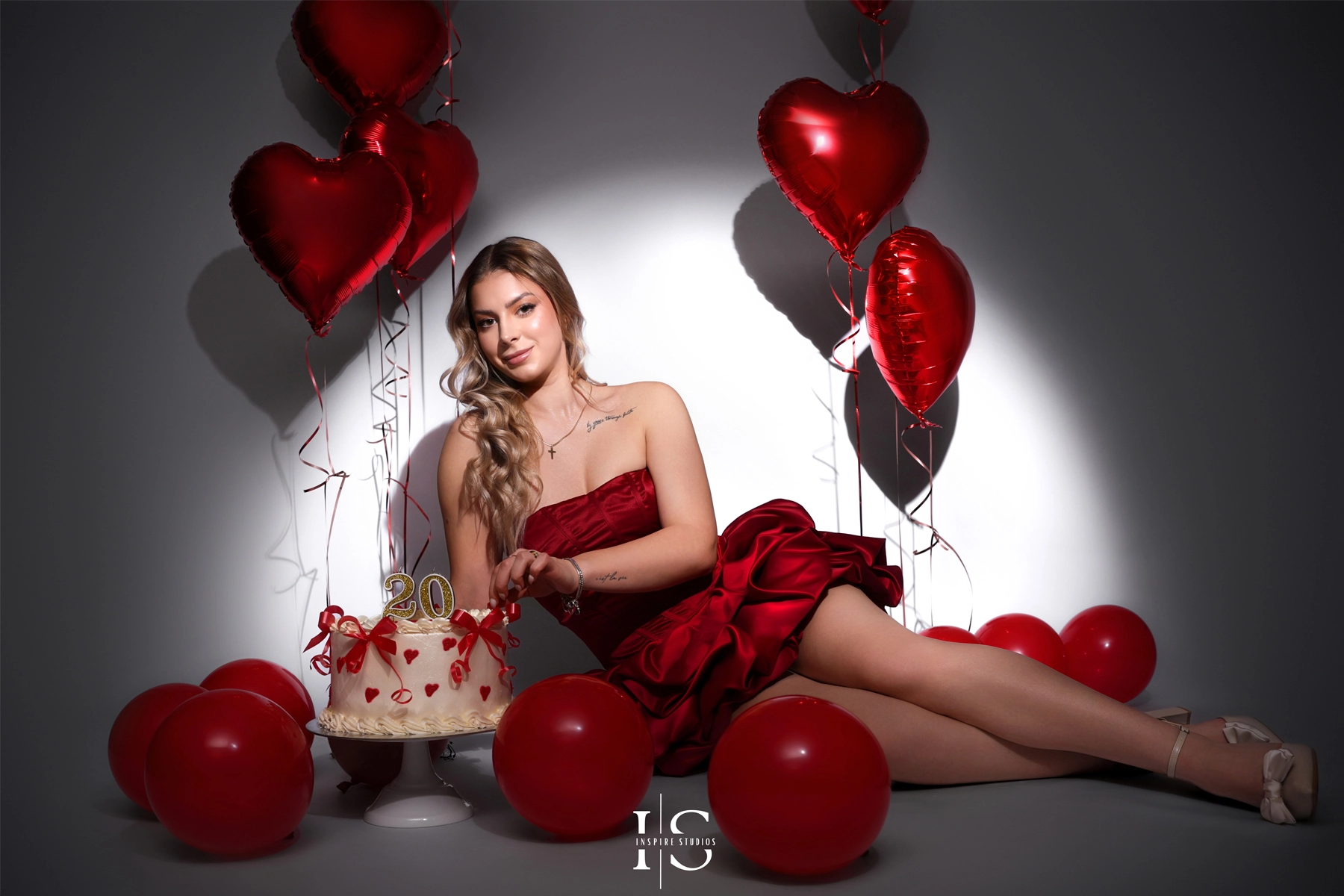 Elegant 20th birthday studio photo session with red heart balloons, roses, and birthday cake, photographed in a professional London-style studio setup.