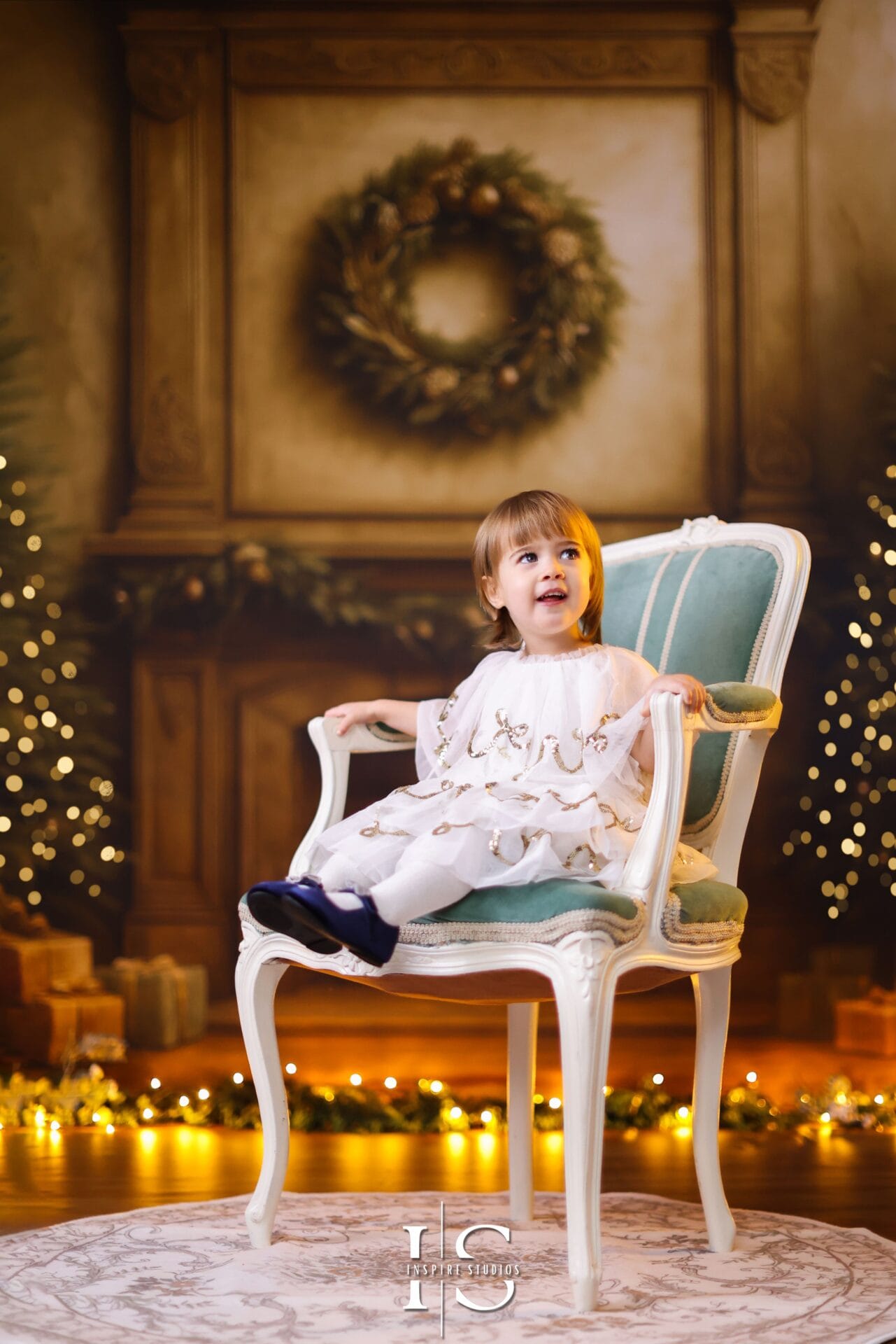 Toddler posing in a classic Christmas studio setting with traditional holiday decorations and warm lighting.