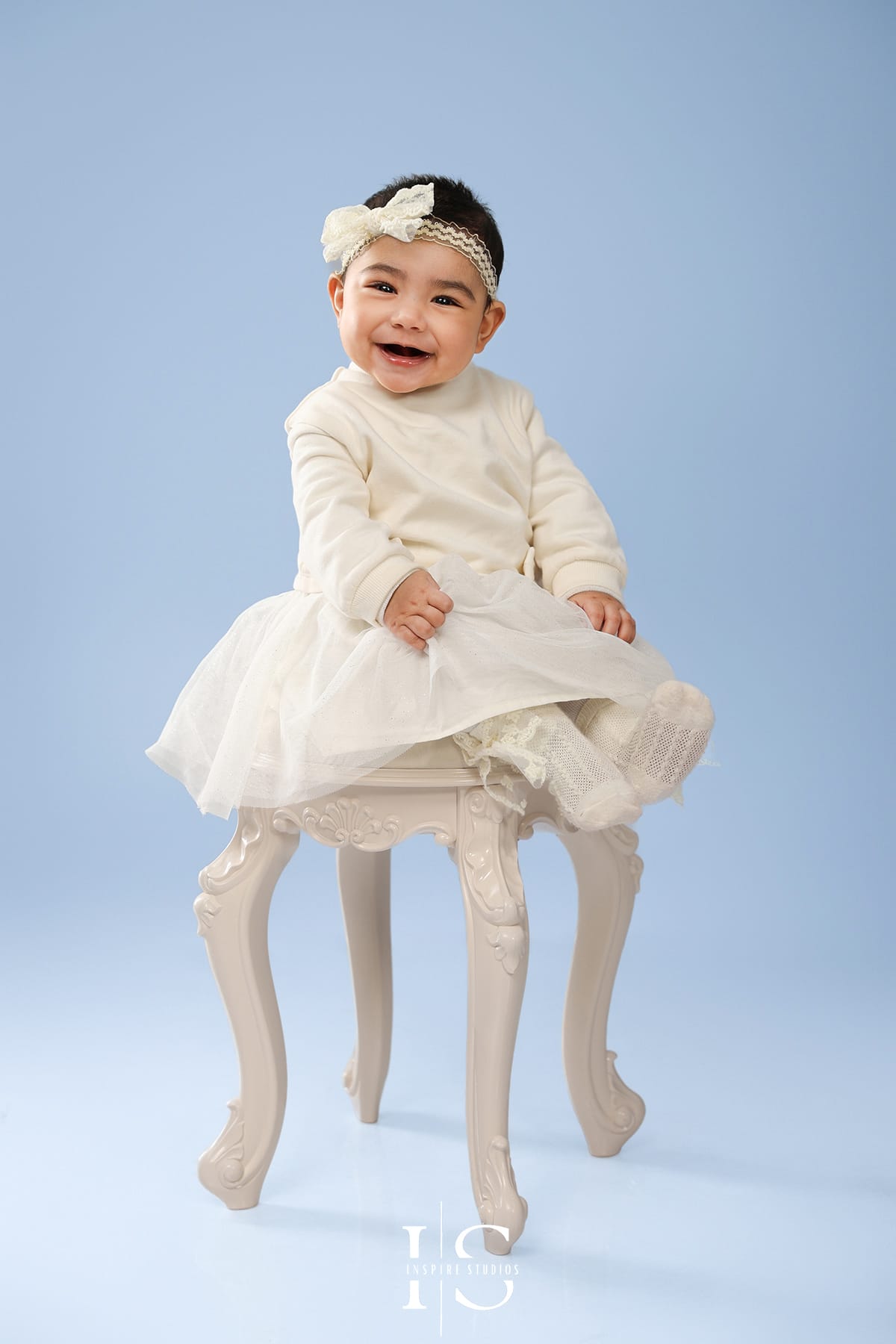 Family studio photo shoot with smiling 7-month-old baby girl sitting on soft blanket with parents in professional indoor photography studio.