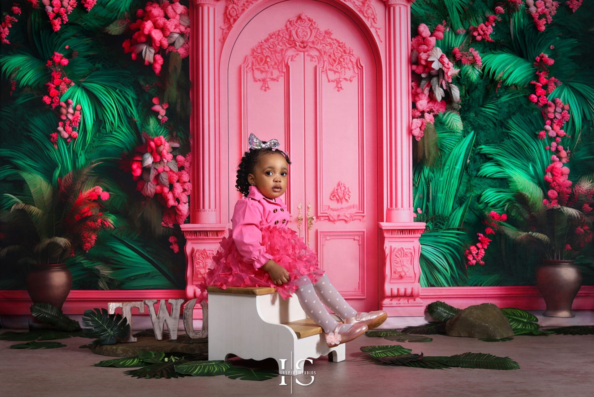 Two-year-old girl smiling during birthday photoshoot with pastel balloons and number 2 decoration
