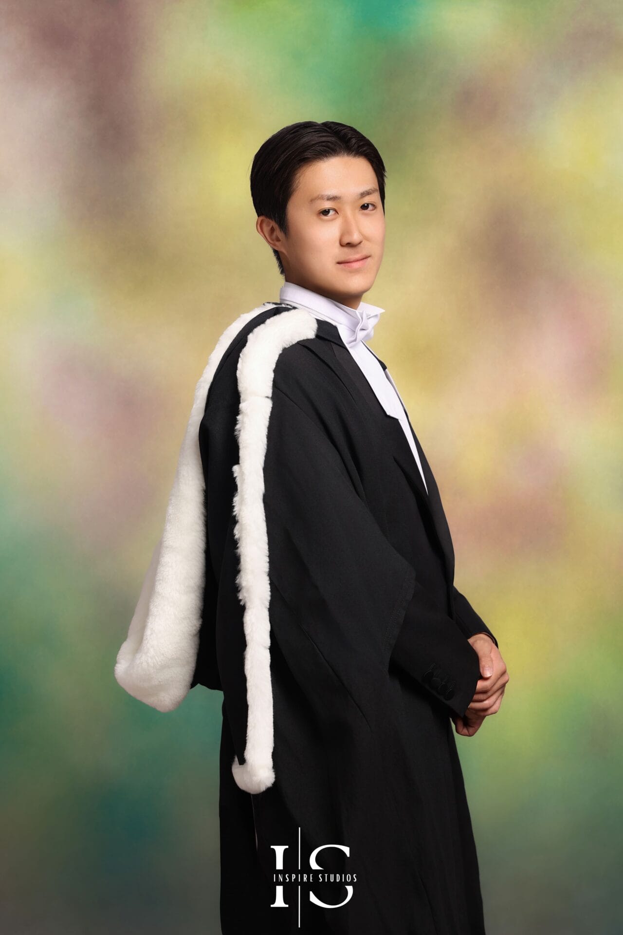 Korean-style graduation portrait in London featuring graduate in formal academic gown with classic painterly studio backdrop and elegant fine art lighting.