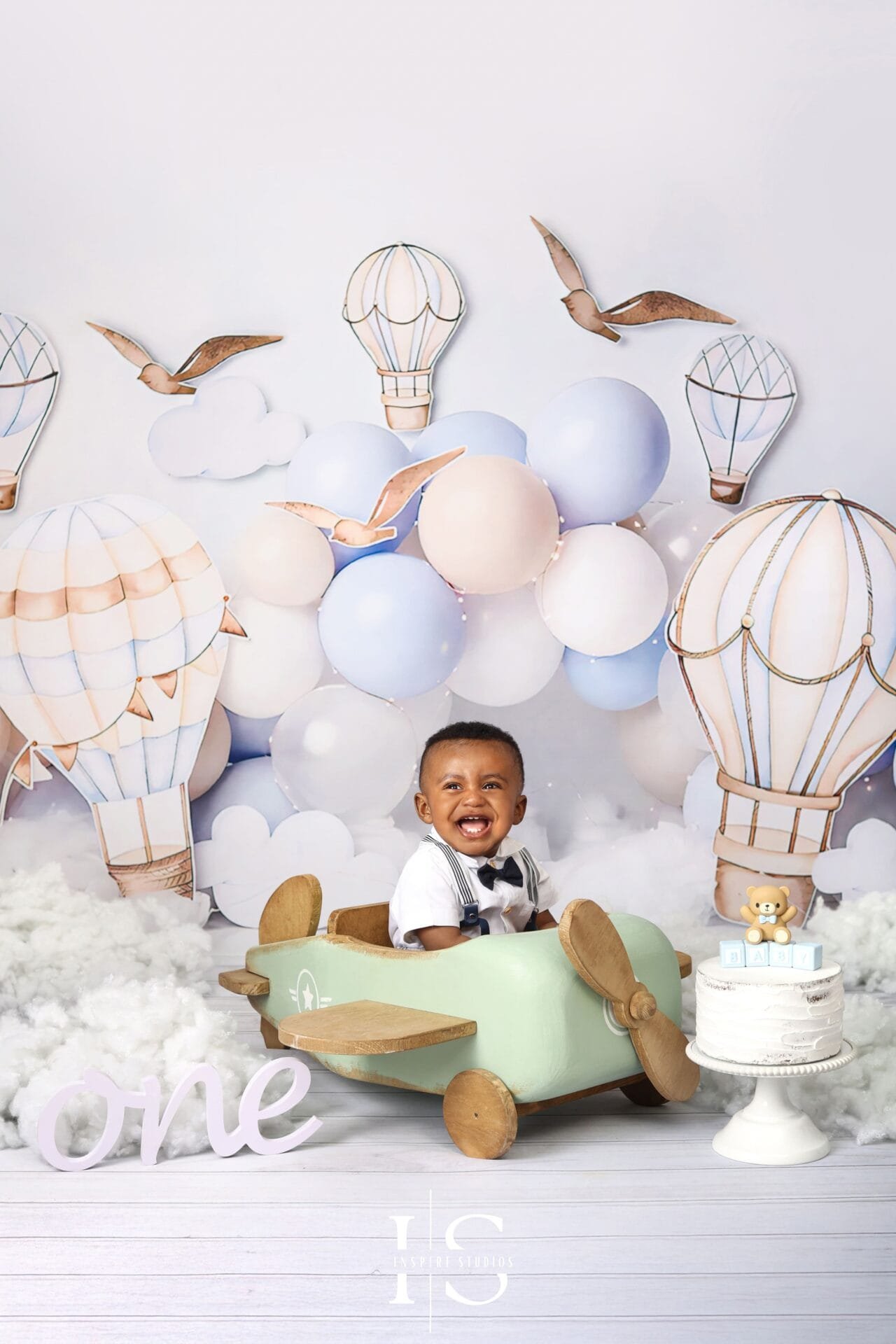 One-year-old child posing with a wooden airplane prop during a first birthday photoshoot in London.