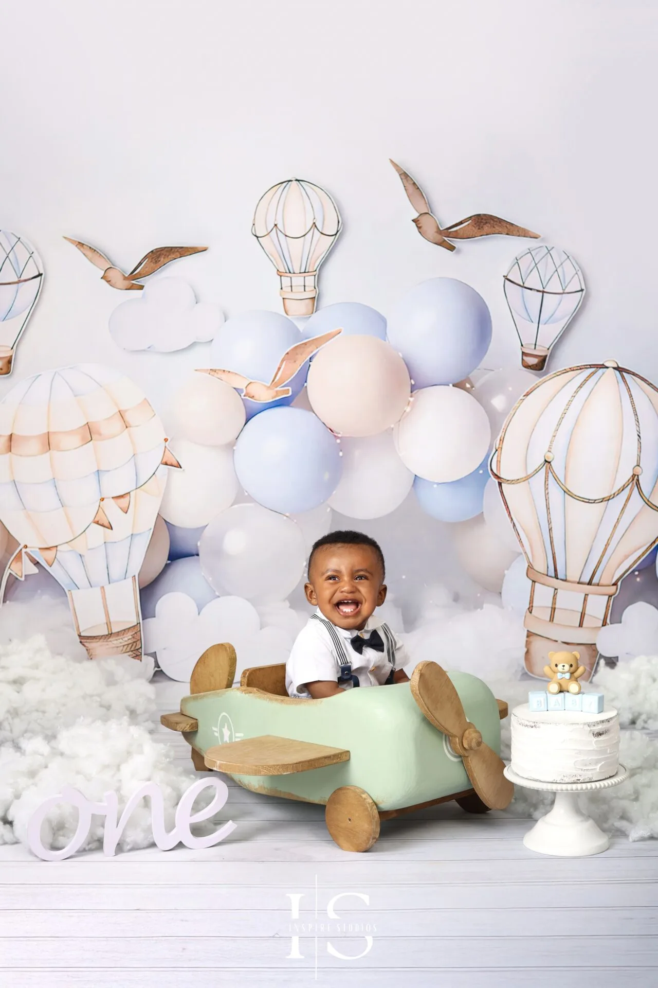 One-year-old child posing with a wooden airplane prop during a first birthday photoshoot in London.